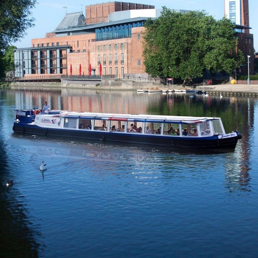 Riverboat cruising on a calm river near modern buildings on a sunny day.