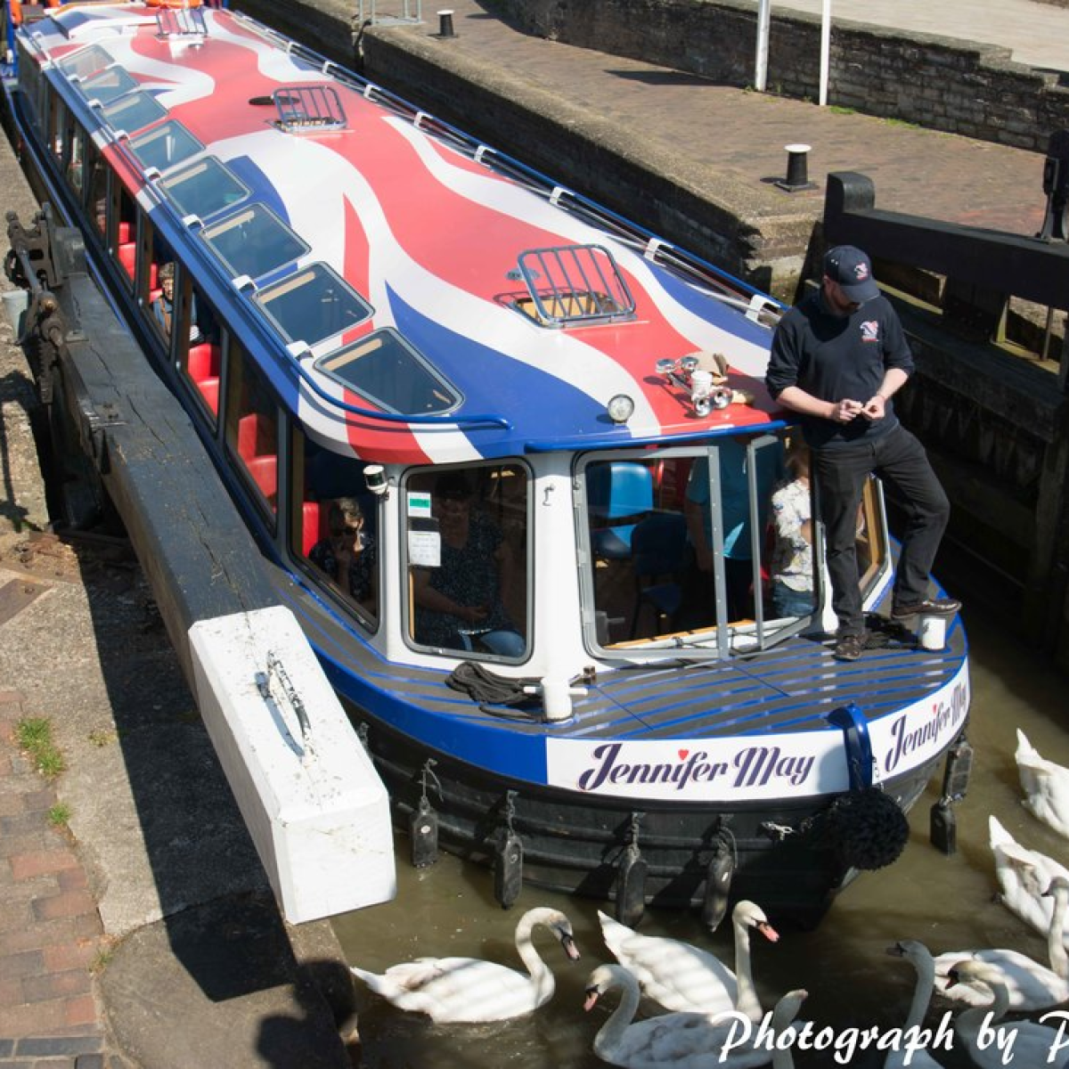 A British flag-themed boat in a canal lock with swans around it.