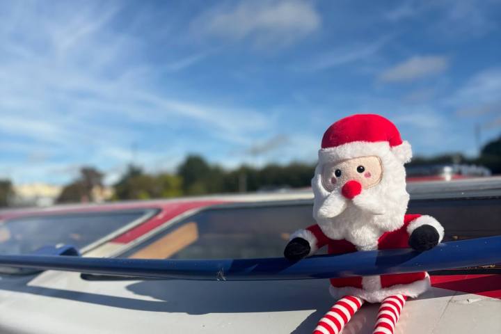 Santa doll on car roof under blue sky with clouds.