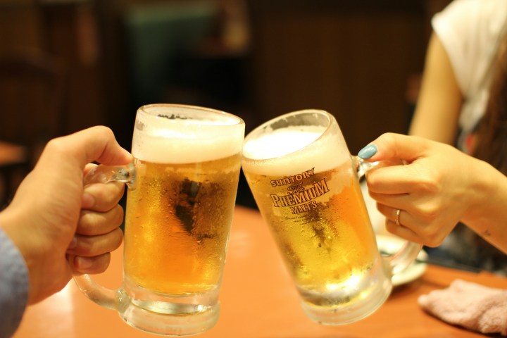 Two hands clinking beer mugs with foam on top.